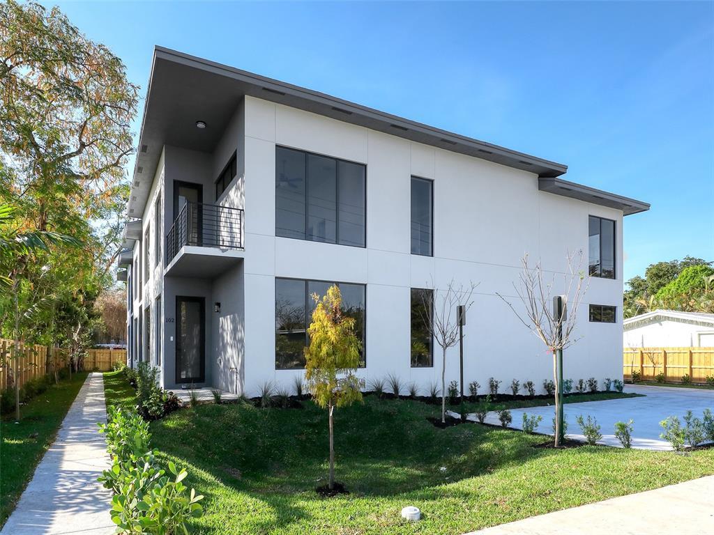 Modern two-story white home with a flat roof, large windows, and landscaped front yard.