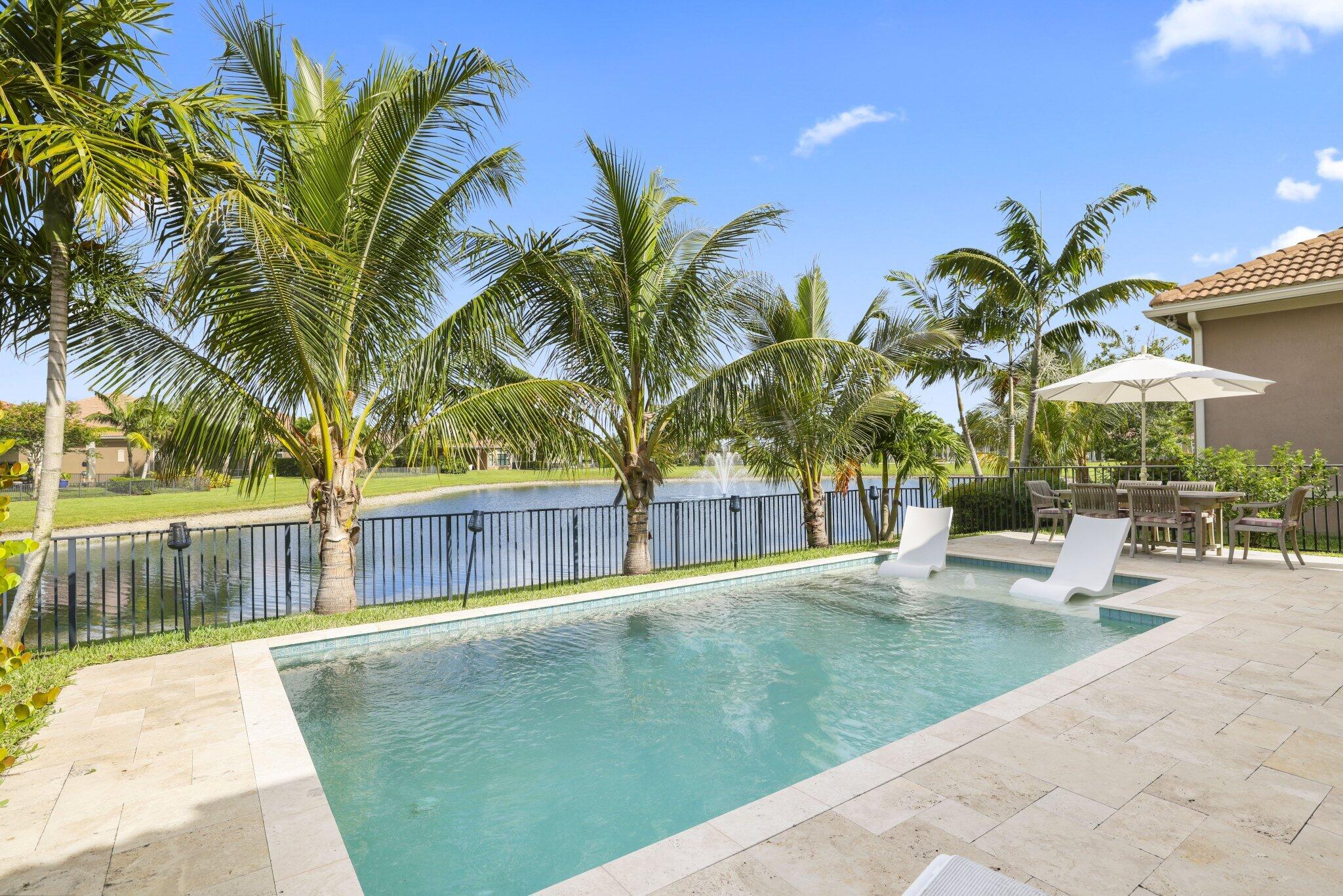 Backyard pool overlooking a lake, framed by palm trees and a stone patio.