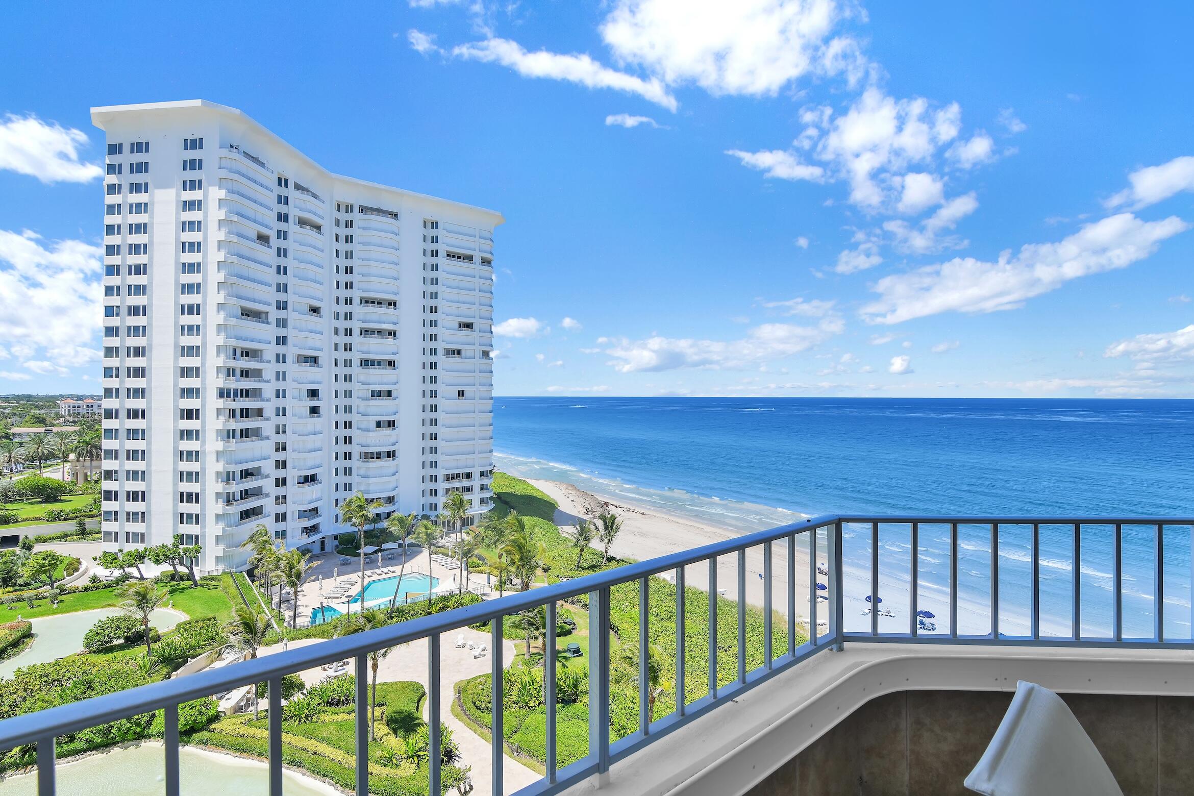 Oceanfront condominium tower beside a sandy beach, seen over a balcony railing.