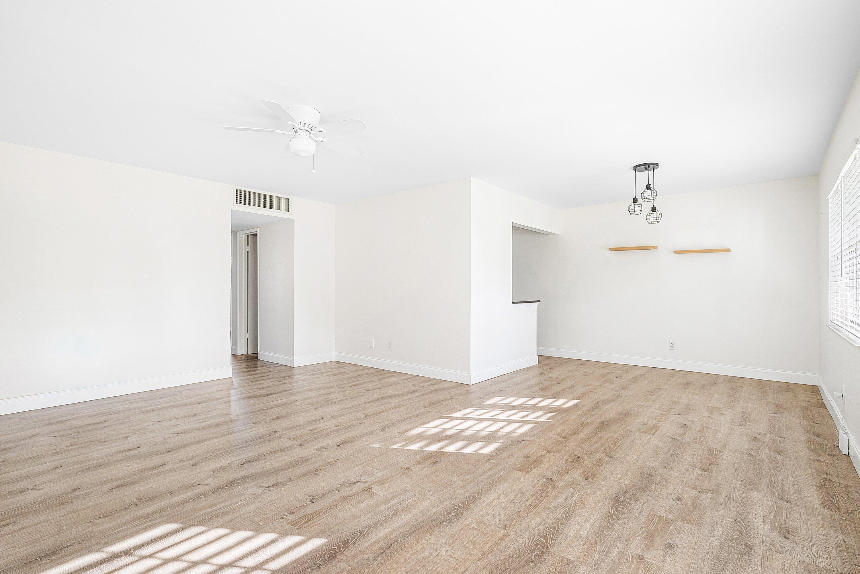 Vacant living and dining area with light wood floors, pendant lights, and sunlight through window blinds.