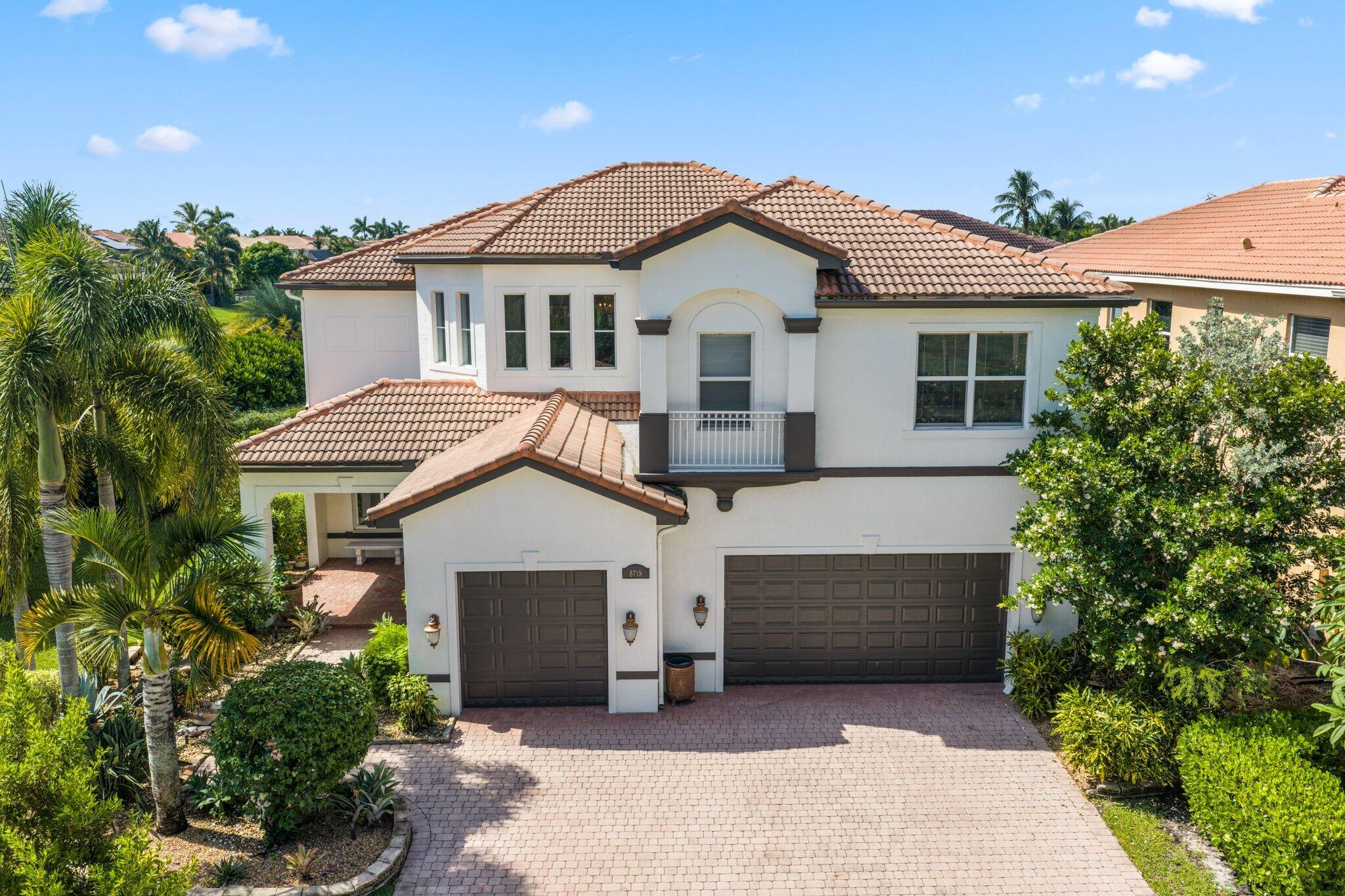 Two-story stucco home with a tiled roof, double garages, and a palm-lined paver driveway.