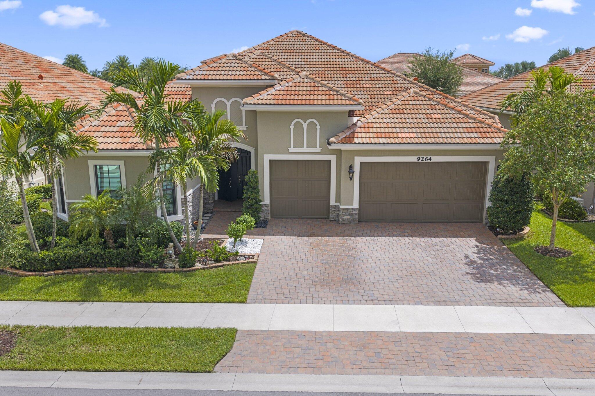 Two-story home with a terracotta tile roof, palm landscaping, and a wide paver driveway.