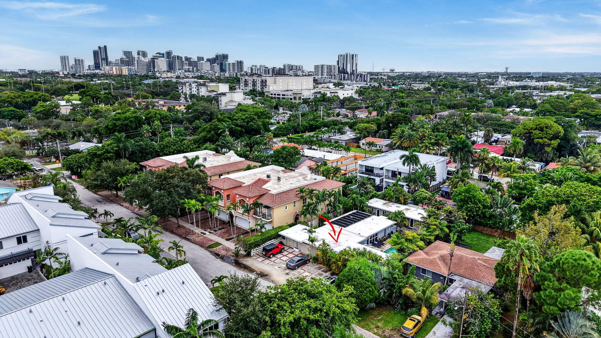 Aerial view of Fort Lauderdale homes and palms, with a red arrow pointing to a white-roofed property.