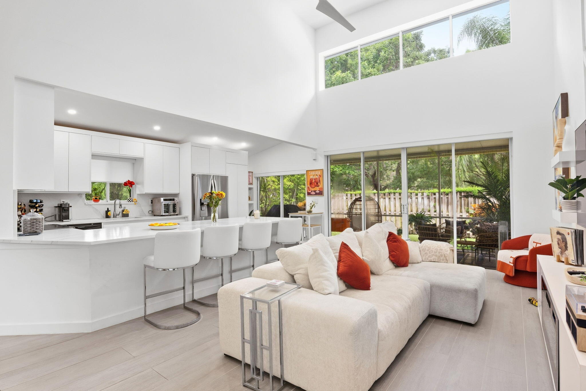 Open-plan living room and kitchen with a white sectional, high ceilings, and sliding doors to a leafy patio.