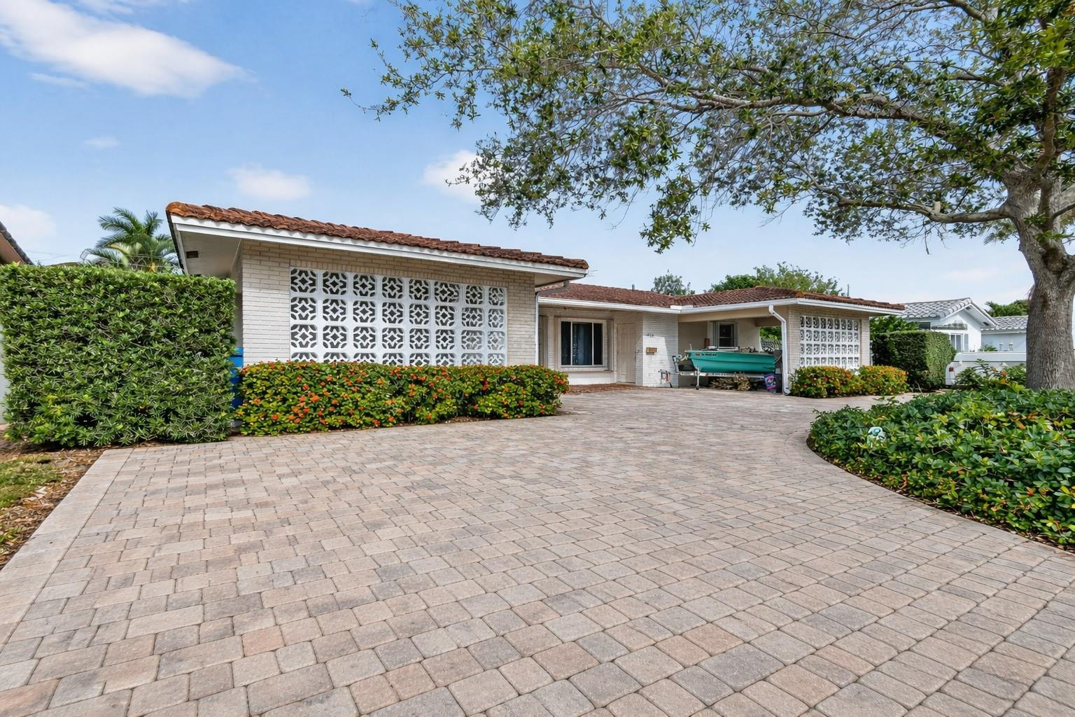 Single-story home with decorative breeze-block walls, a broad paver driveway, and tropical landscaping.