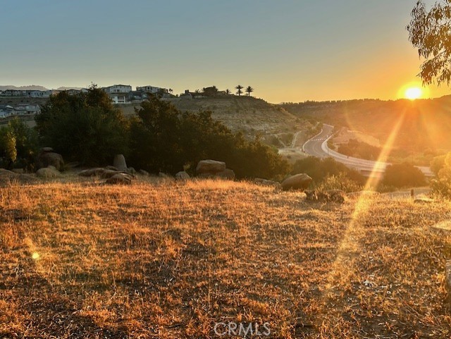 Vacant Chatsworth land with dry grass, hillside homes, a winding road, and sunset.