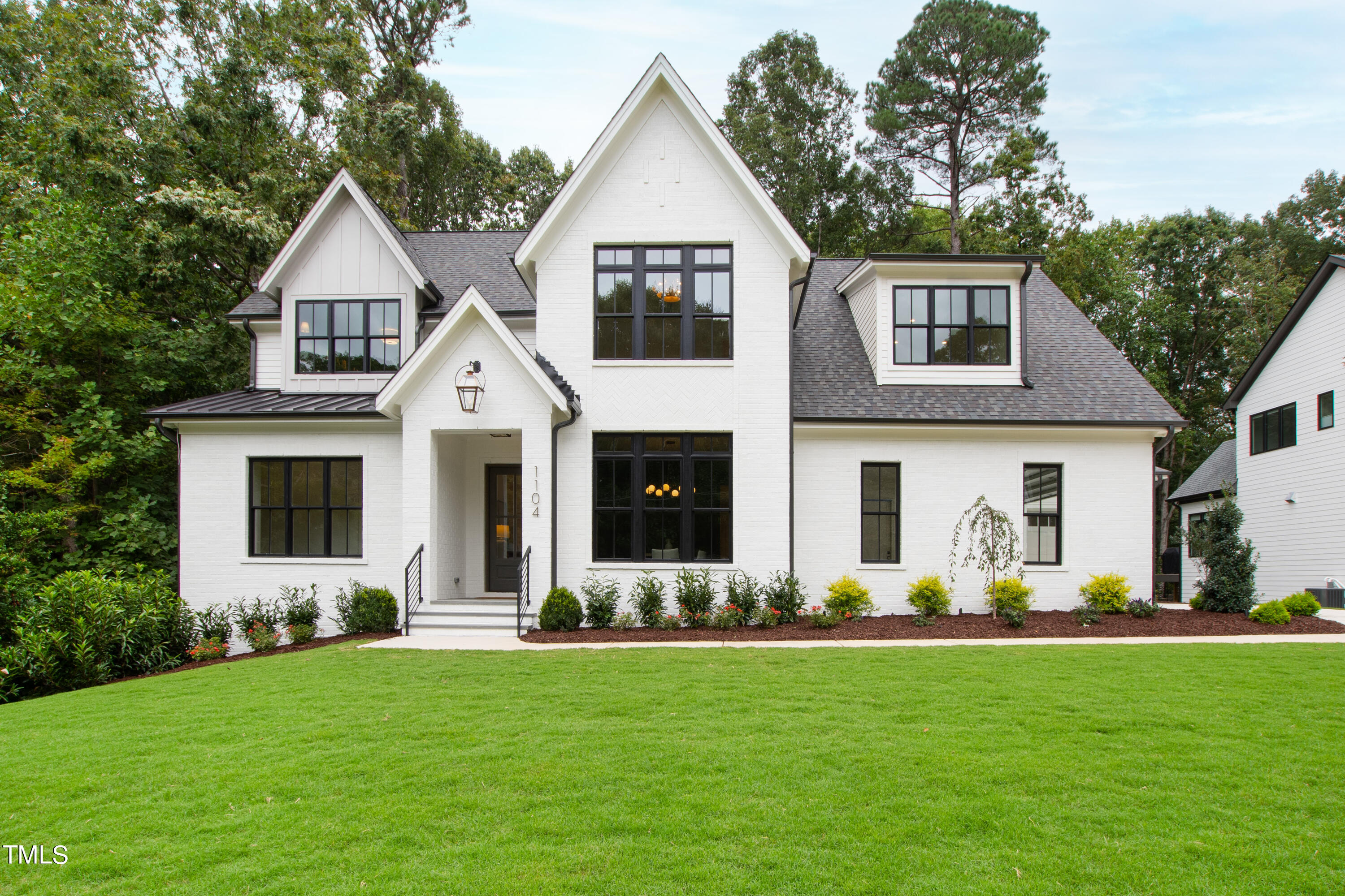 White brick house with steep gables, black-framed windows, and a broad green lawn.