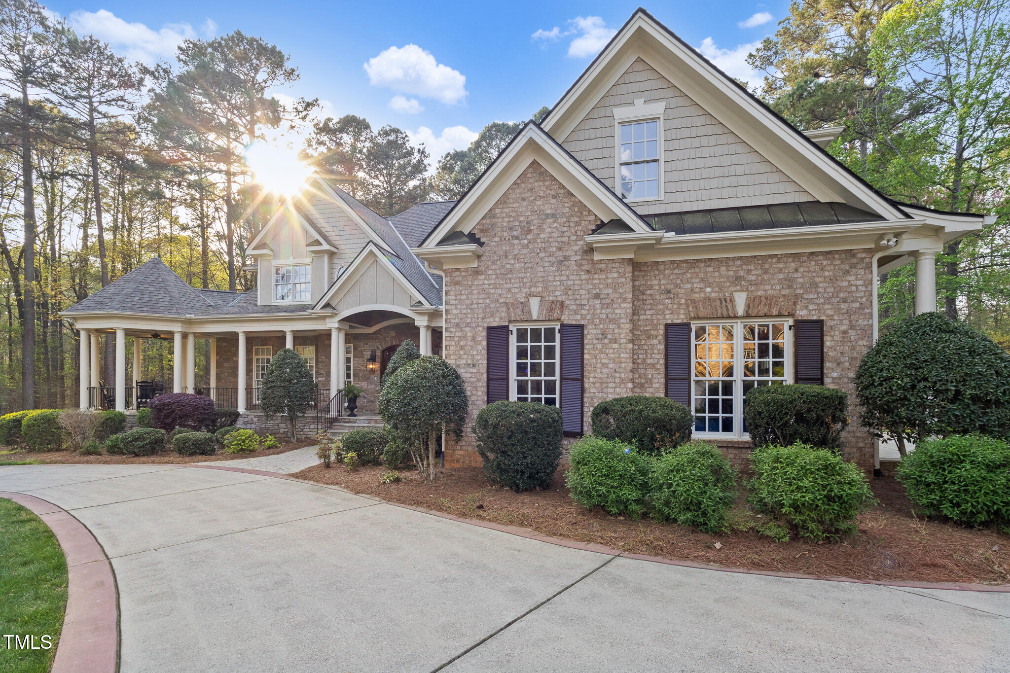 Two-story brick house with steep gables, covered porch, landscaped shrubs, and a curved driveway.