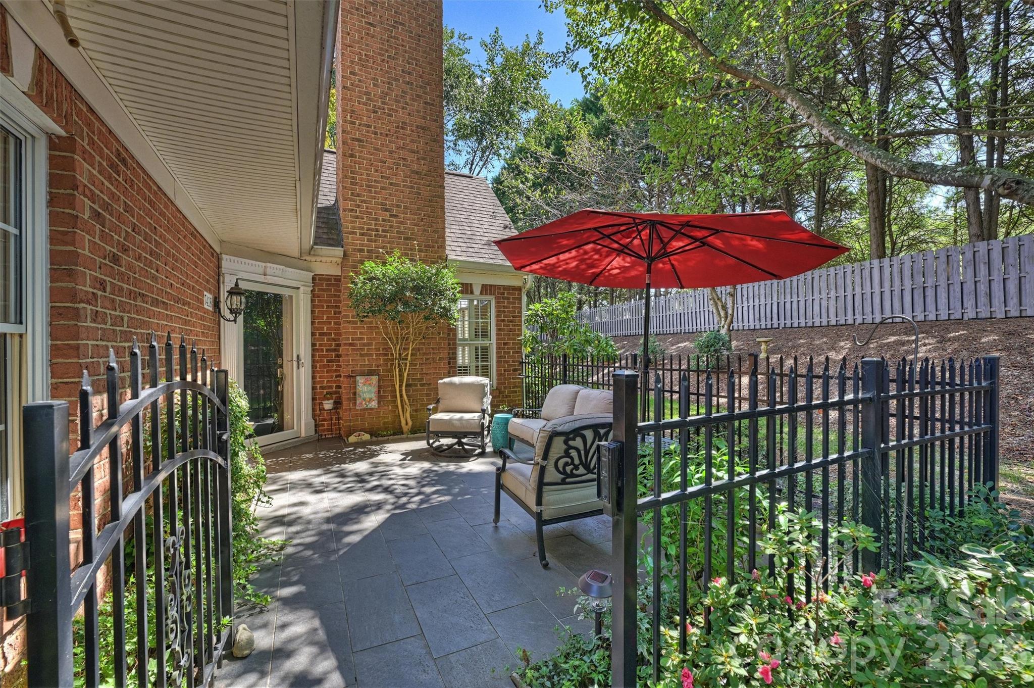 Brick home's fenced patio with cushioned seating beneath a large red umbrella.