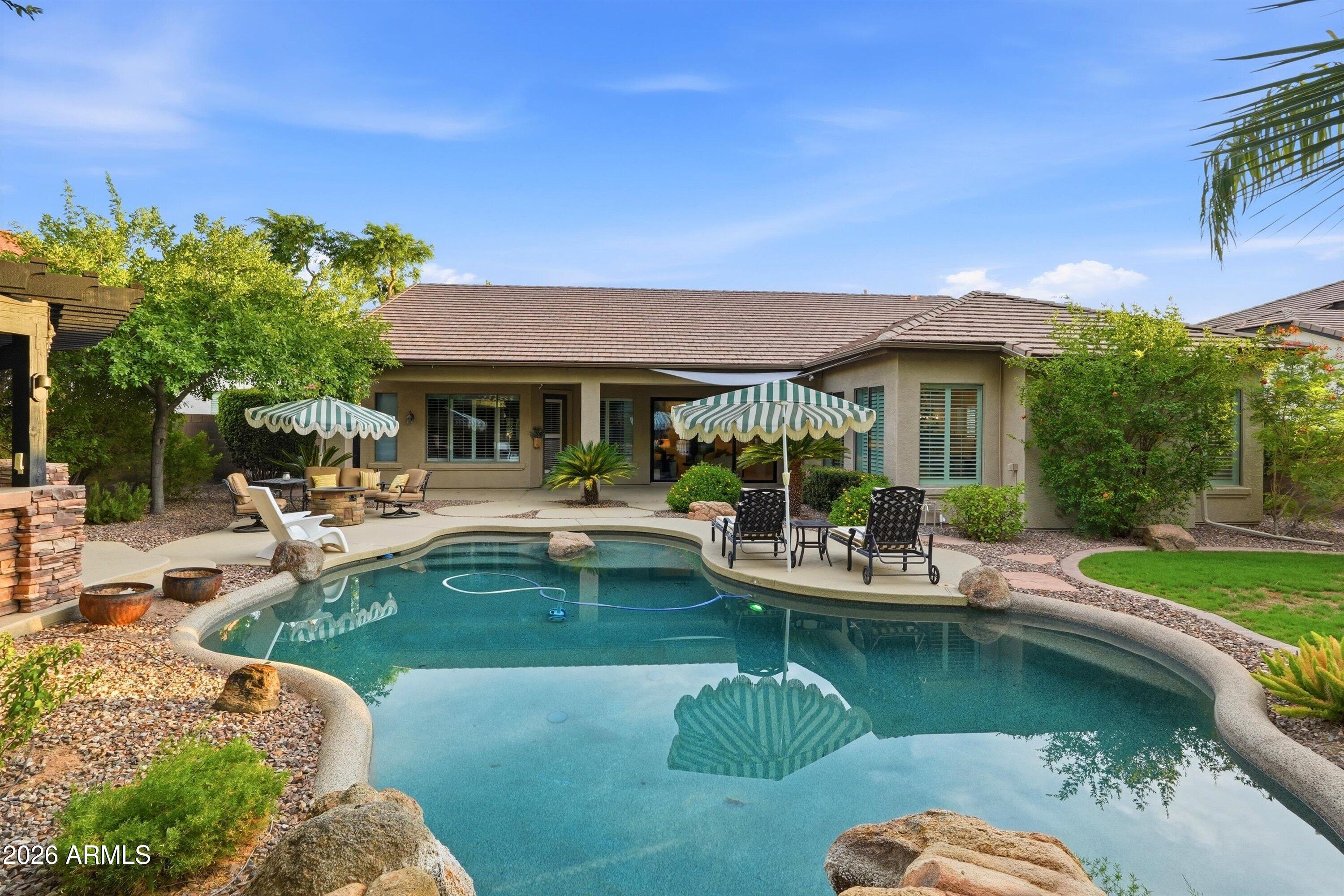 Backyard pool beside a single-story home, with striped umbrellas and shaded patio seating.