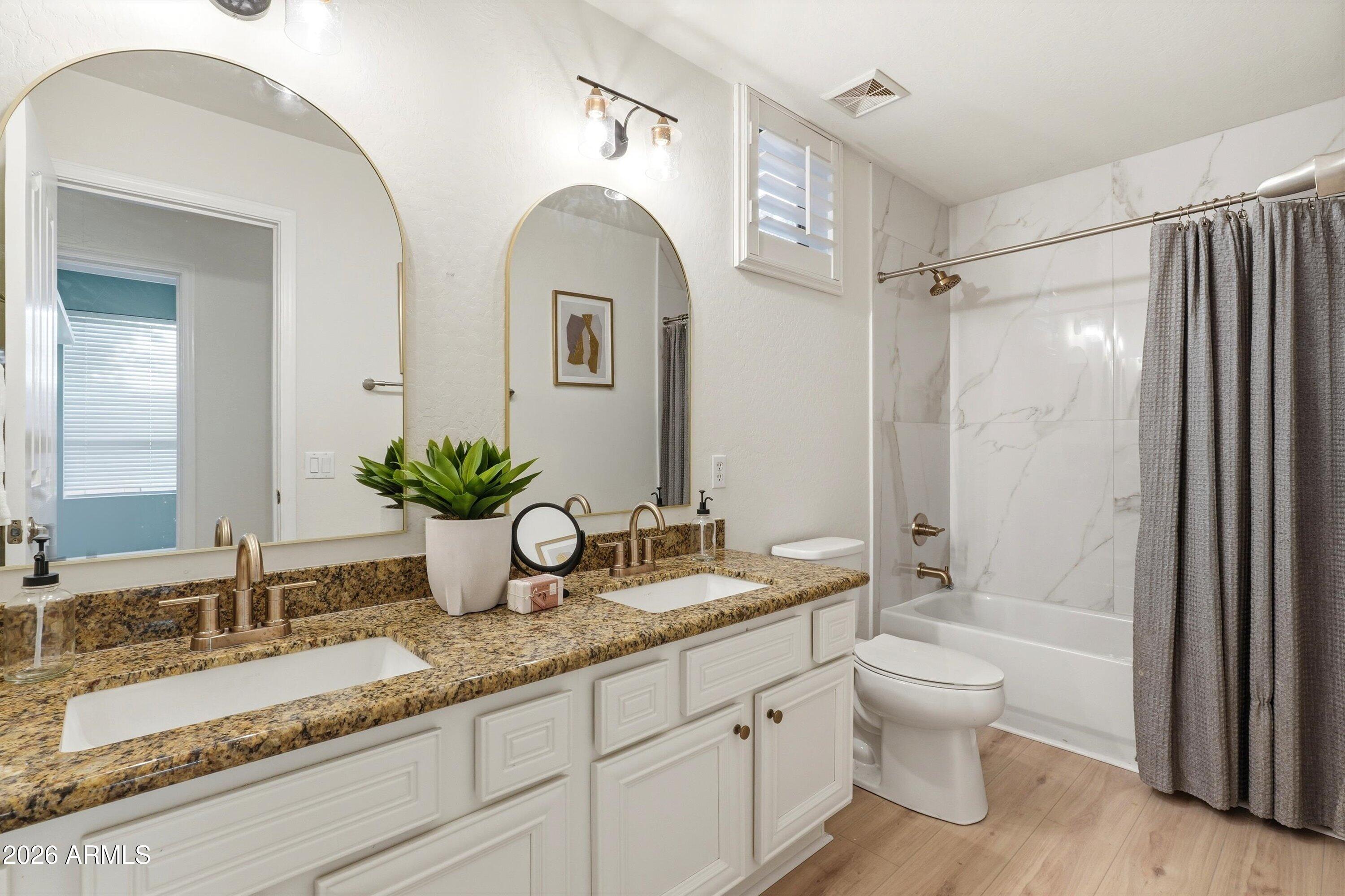 Bathroom with a double-sink vanity, granite countertop, and marble-look tub surround.