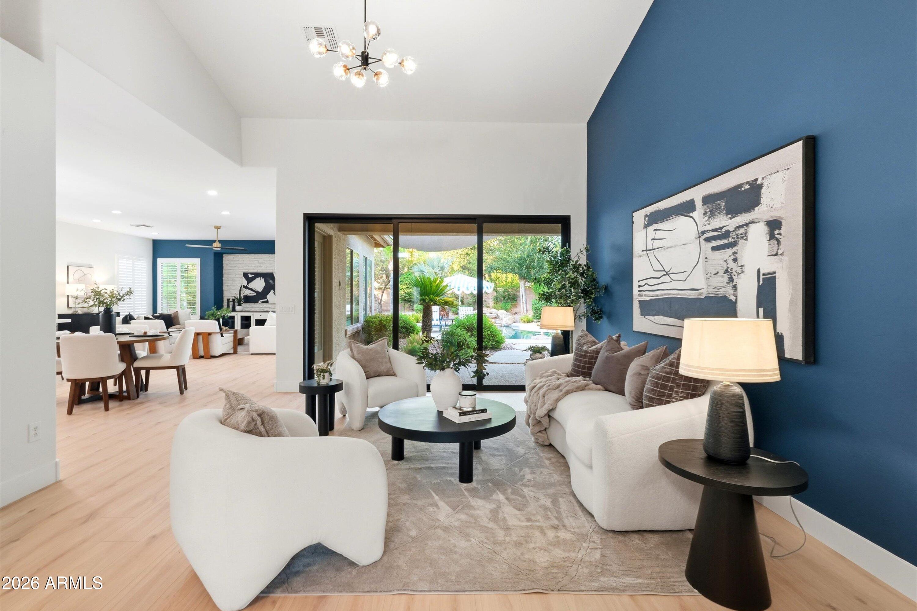 Staged living room with white sofas and a blue accent wall, opening to a landscaped backyard and pool.