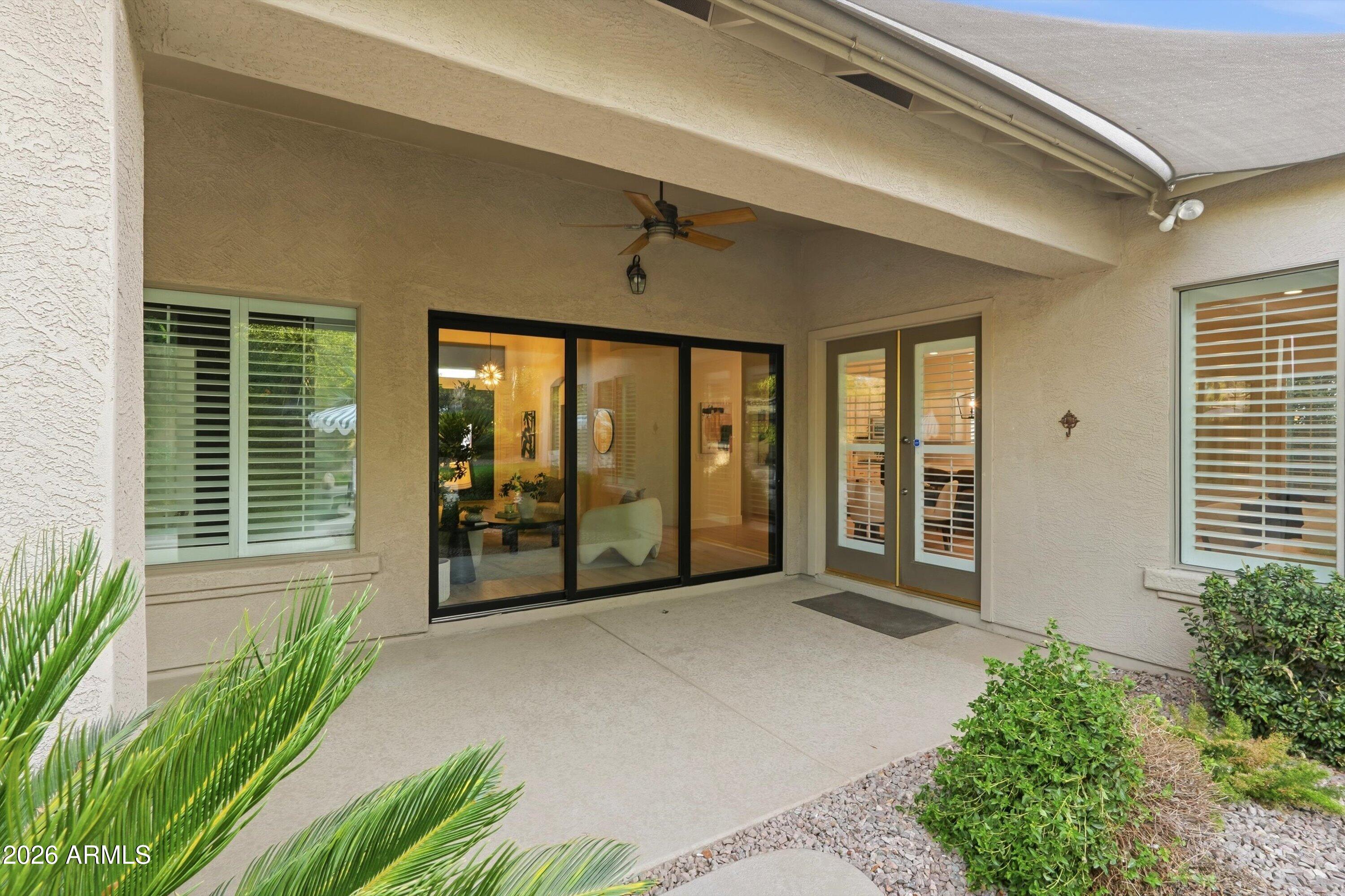 Covered patio with a ceiling fan and black-framed sliding glass doors, bordered by desert landscaping.