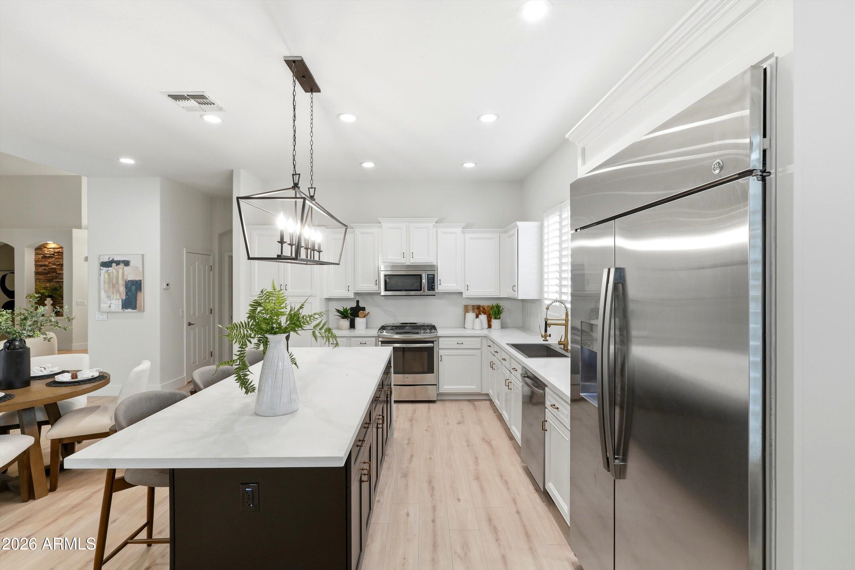 Open kitchen with a large island, white cabinets, stainless appliances, and an adjoining dining area.