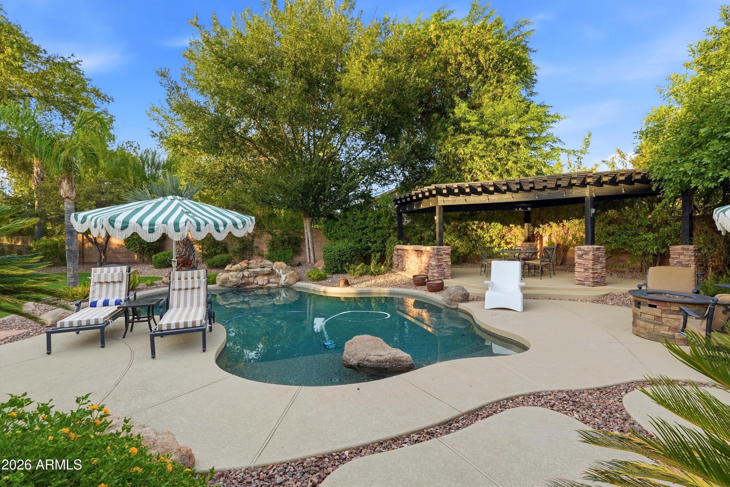 Backyard pool with a striped umbrella, lounge chairs, and a covered pergola.