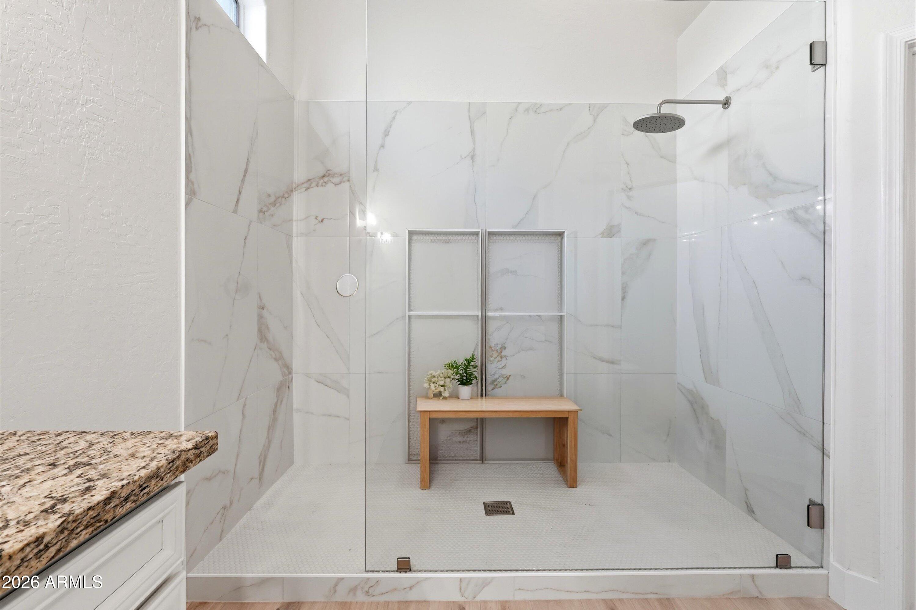 Walk-in shower with marble-look tile, glass enclosure, rainfall showerhead, and recessed niches.