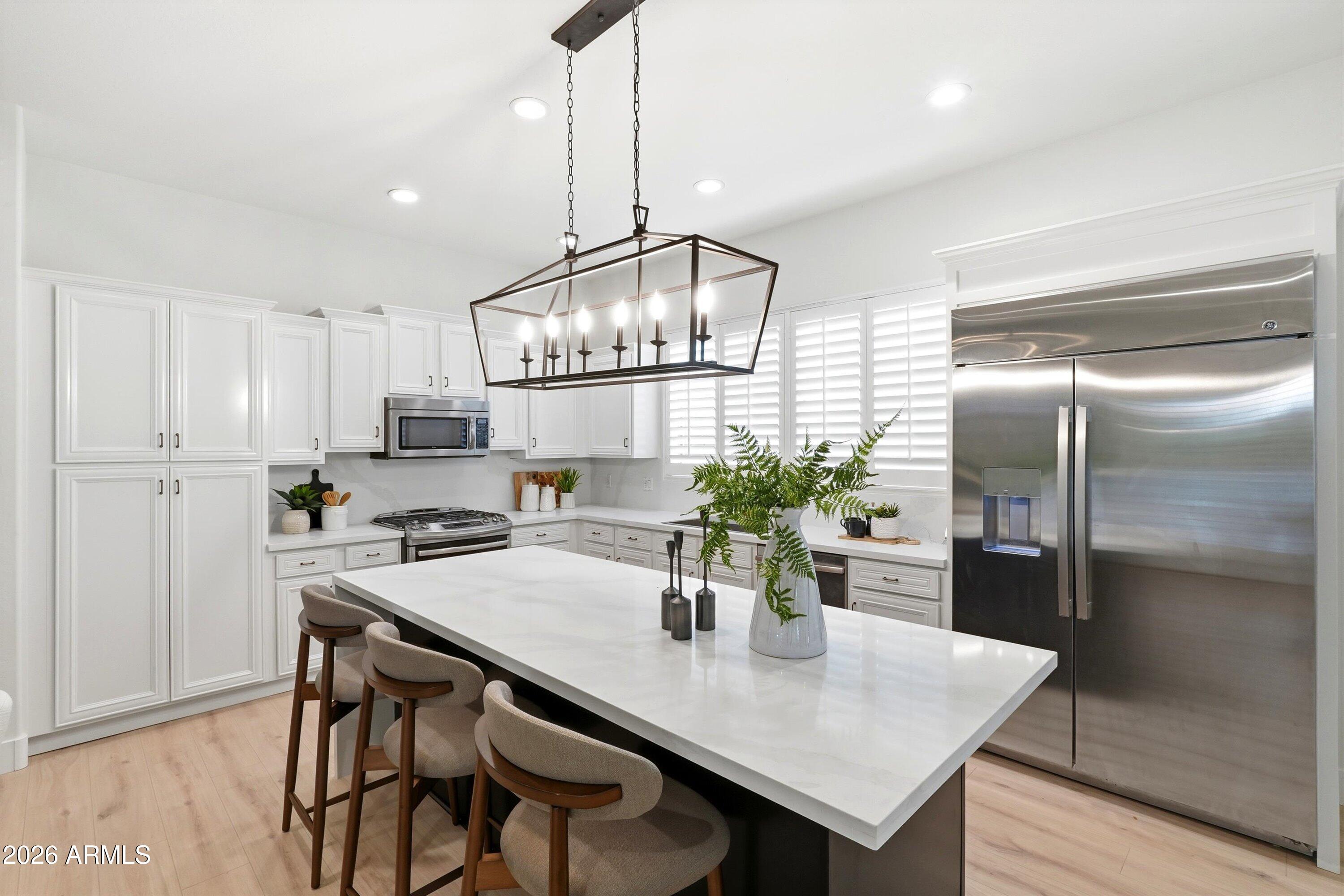 Bright white kitchen with a large island, bar stools, stainless steel appliances, and a geometric pendant light.