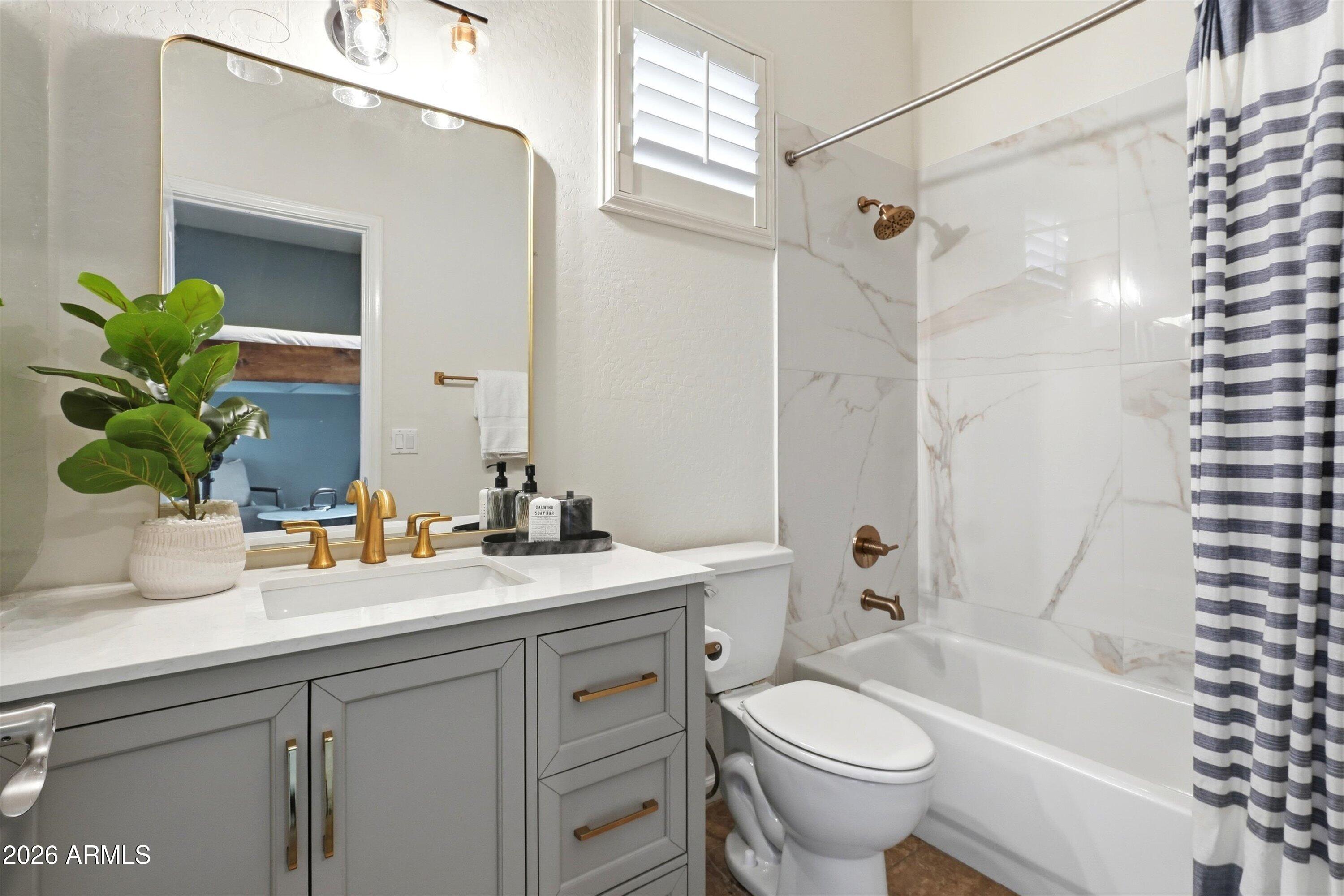 Bathroom with gray vanity, gold fixtures, and a marble-look tub surround.