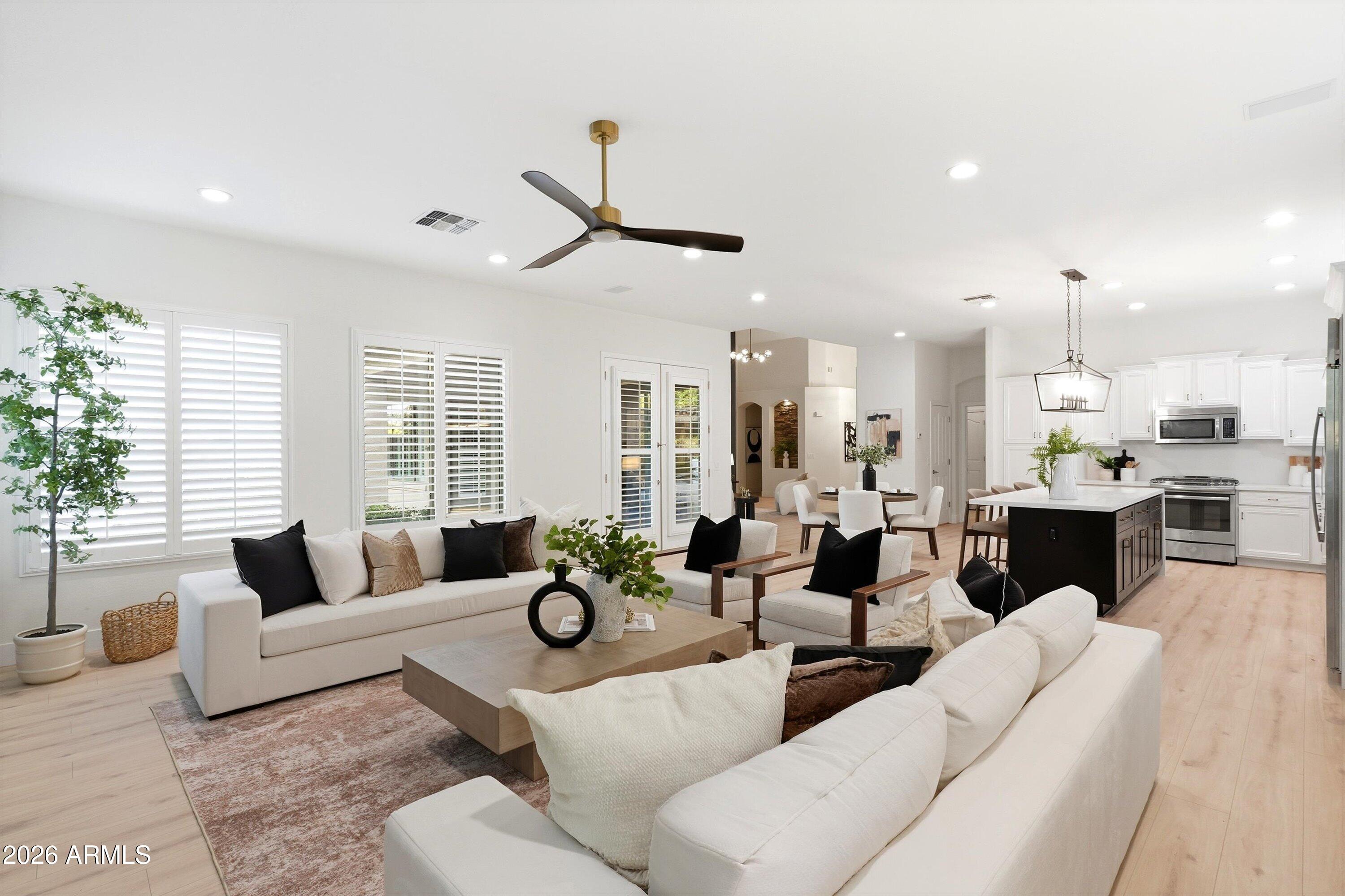 Open-plan living room with white sofas, shuttered windows, and a kitchen with a dark island.