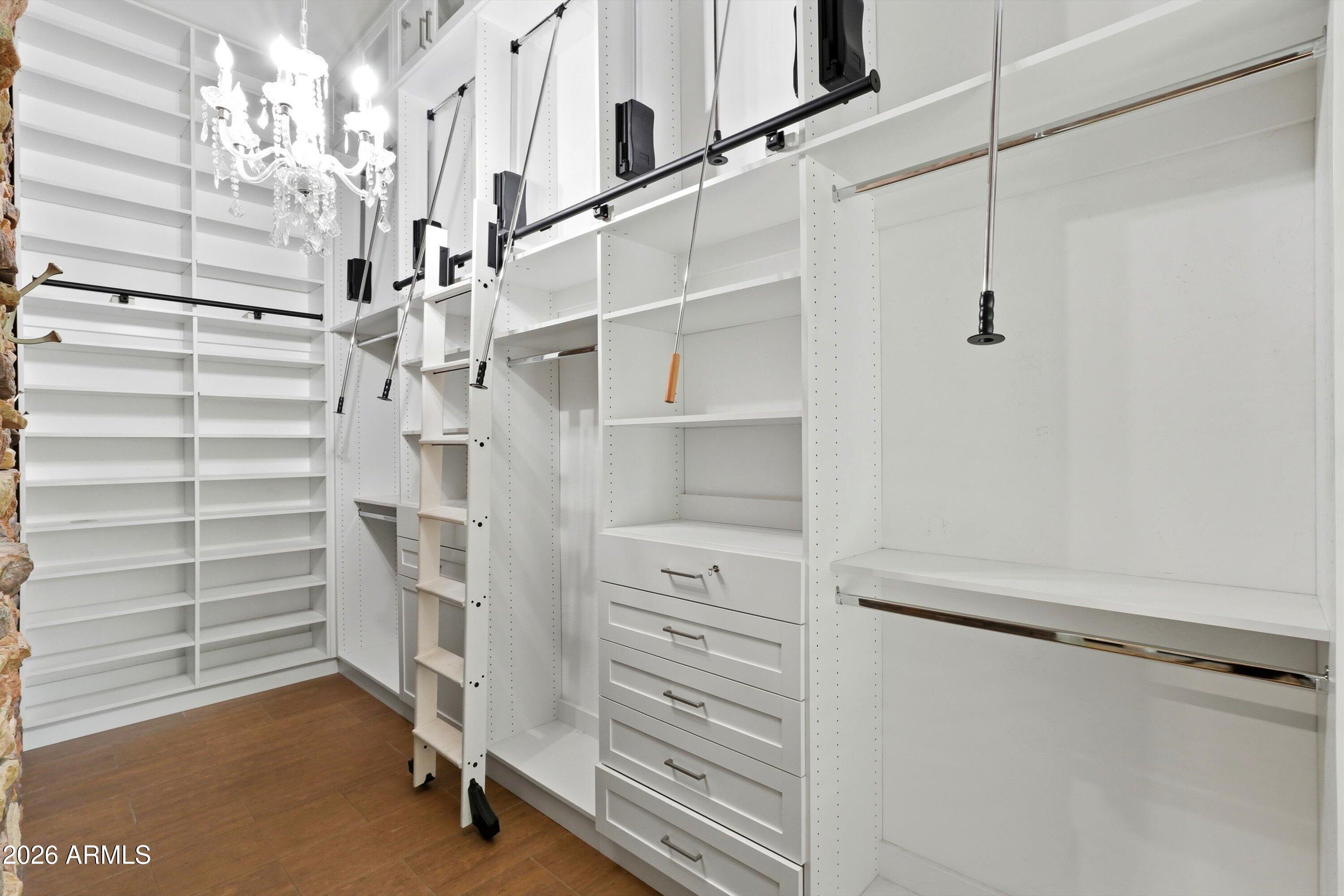 Walk-in closet with extensive white built-ins, rolling ladders, and a crystal chandelier.