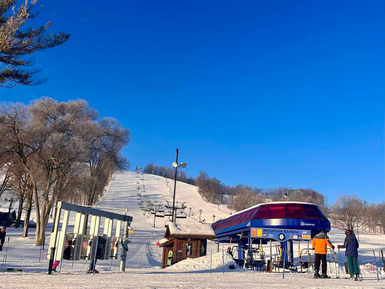 Snow-covered ski slope with chairlifts and a Mountain Express station at the base.