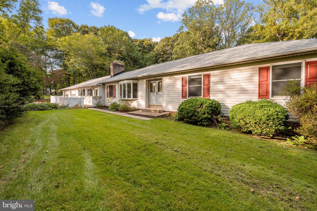 Single-story house with red shutters, a broad lawn, and autumn trees.