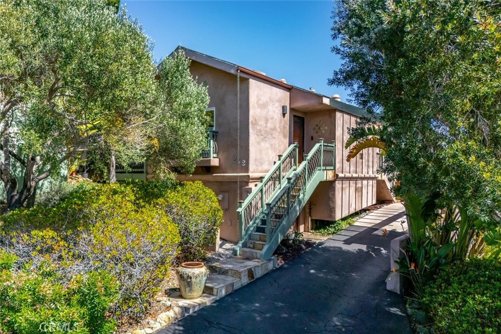 Tan stucco residence with green-railed exterior stairs, paved driveway, and mature landscaping.