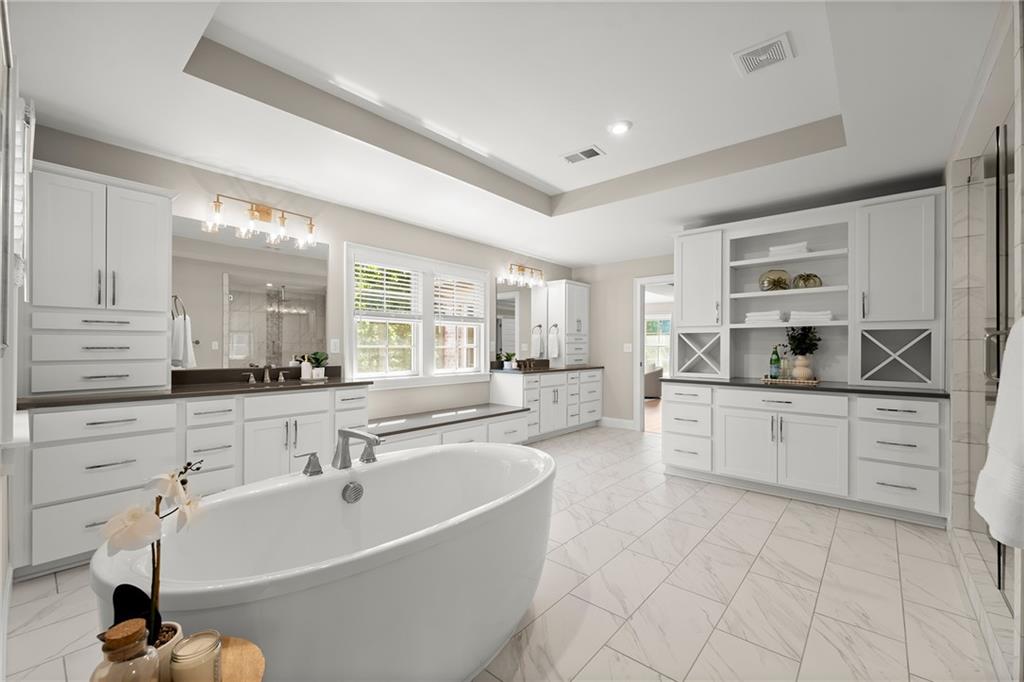 Bright primary bathroom with a freestanding soaking tub, white cabinetry, and marble-look tile flooring.