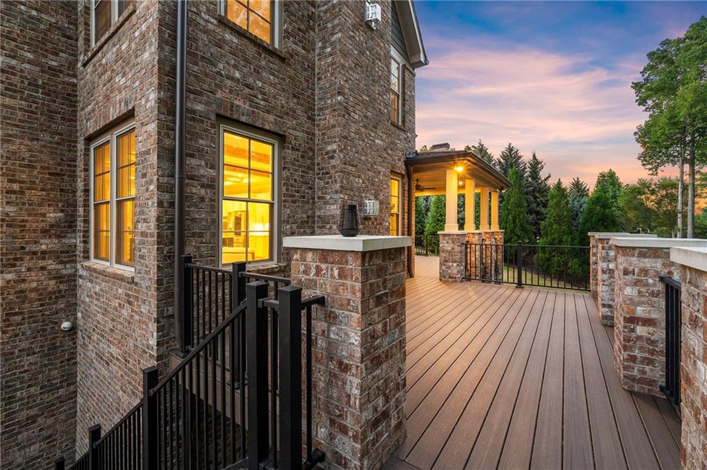 Elevated wood deck beside a brick house, with black railings and a covered porch at dusk.