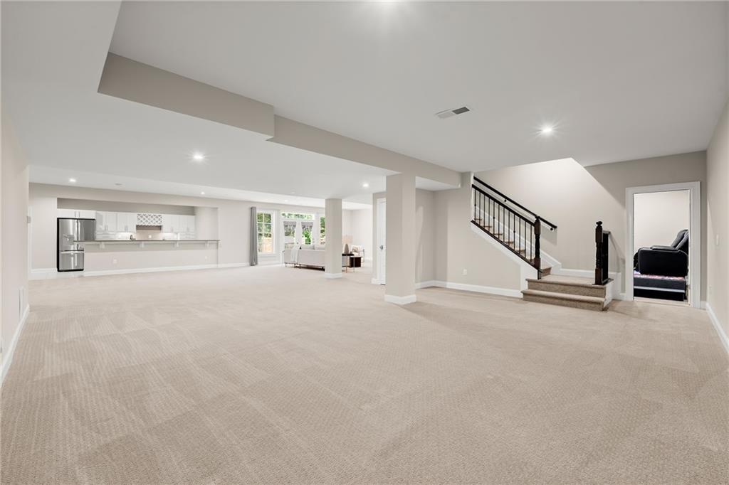 Spacious carpeted lower-level living area with an open kitchen and staircase.
