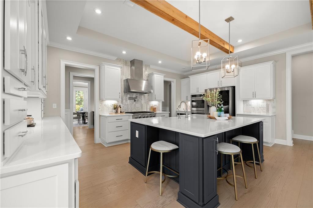 Kitchen with white cabinetry, a navy island, four bar stools, and a timber ceiling beam.