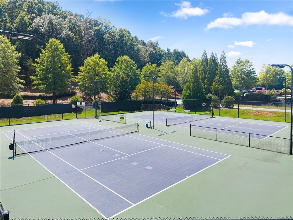 Fenced outdoor tennis courts with multiple nets and a wooded backdrop.