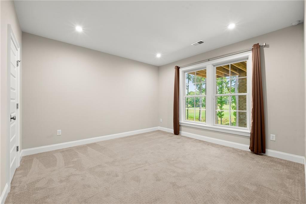 Empty carpeted bedroom with a large curtained window overlooking a lawn and trees.