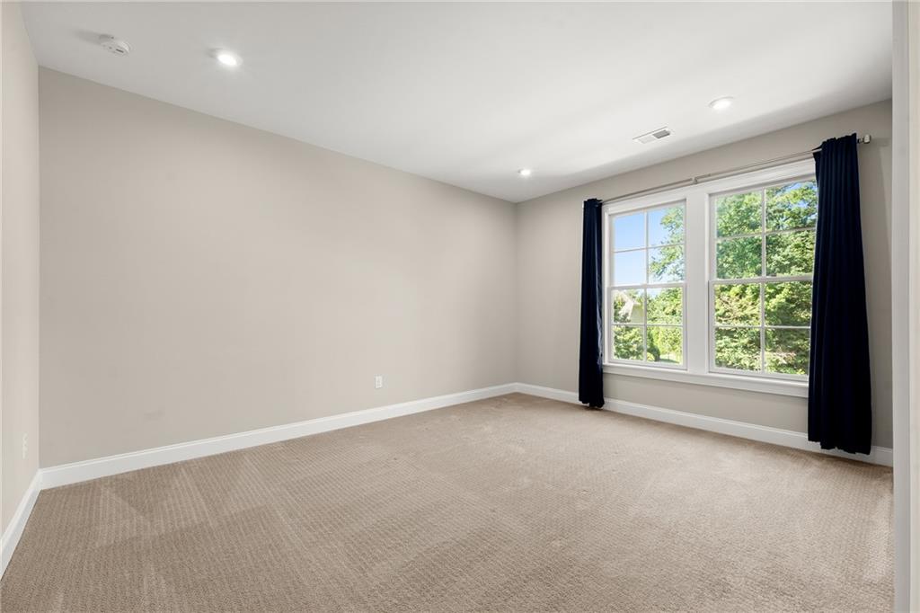 Empty carpeted bedroom with a large window overlooking leafy trees and dark curtains.