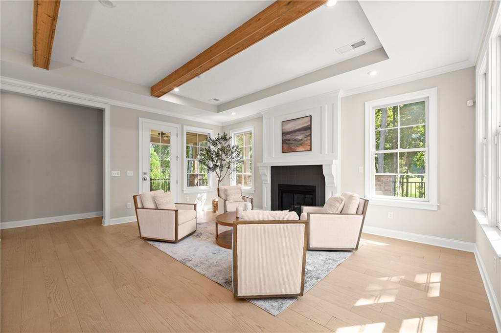 Staged living room with exposed wood beams, a white fireplace, and large windows.