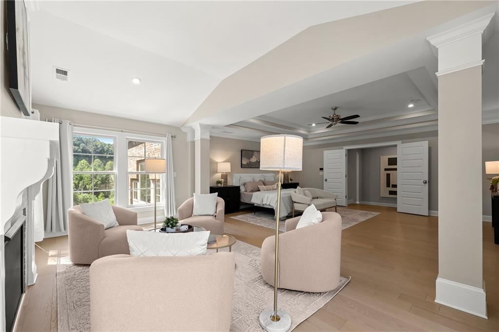 Staged living room with pale pink armchairs, fireplace, and an adjoining bedroom.