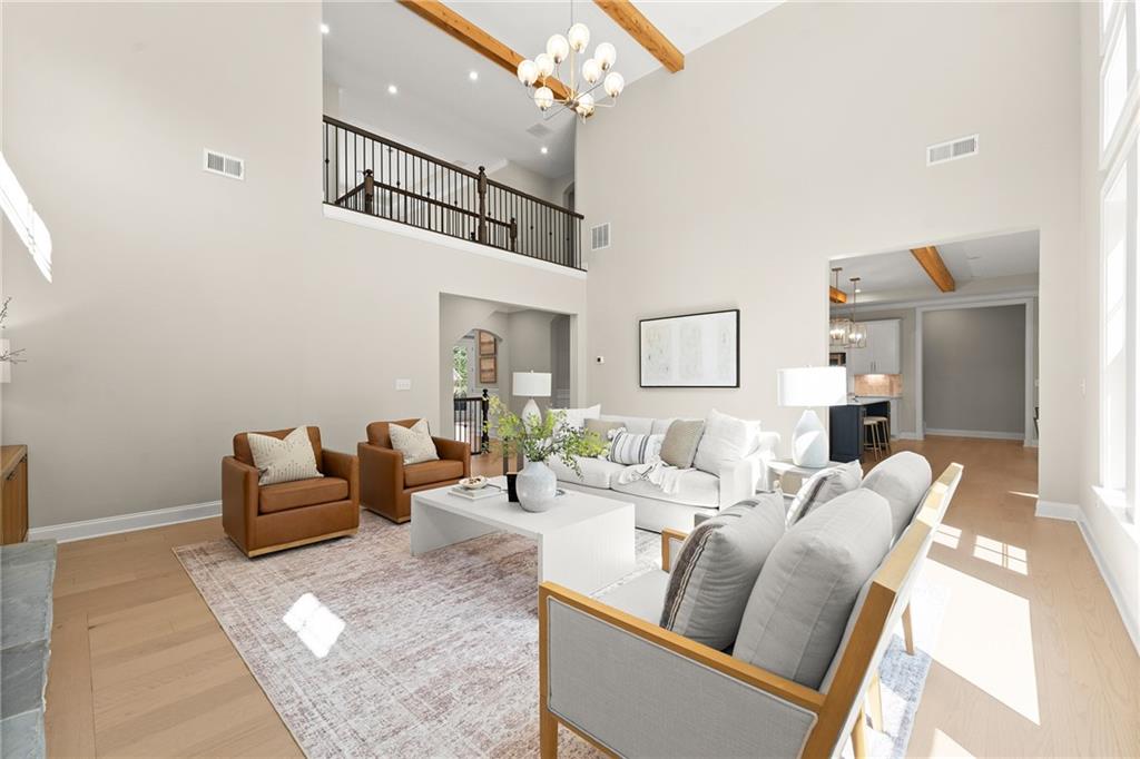 Double-height living room with white sofas, leather armchairs, exposed wood beams and an upstairs balcony.