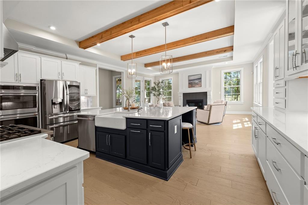 Open kitchen with a navy island, stainless steel appliances, and wood ceiling beams beside a bright living area.