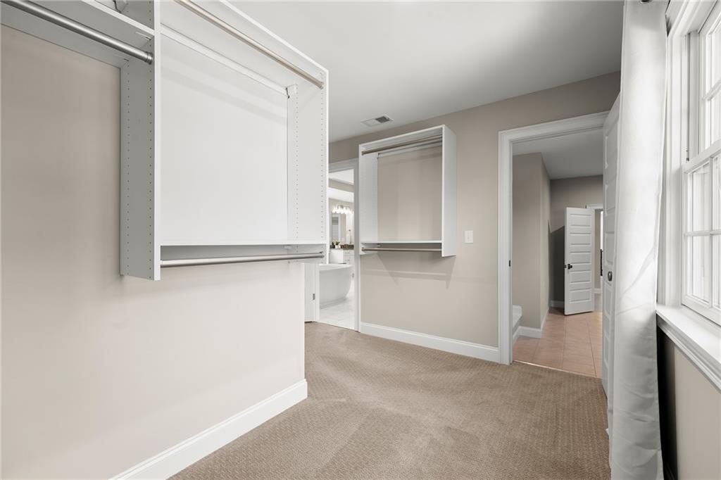 Walk-in closet with white built-in shelving, beige carpet, and a large curtained window.