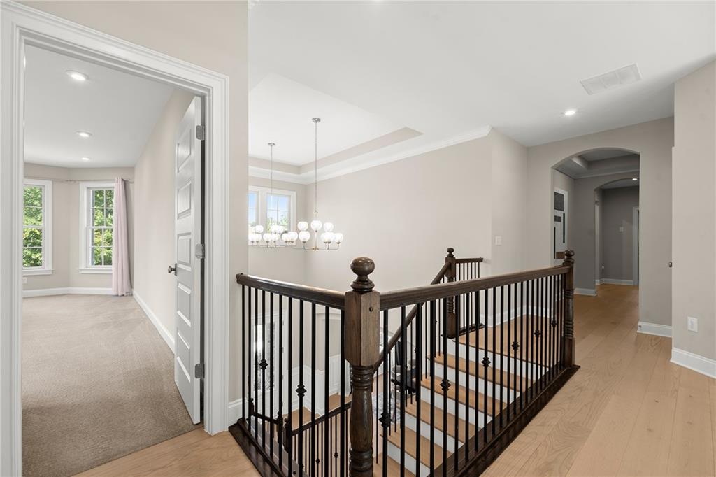 Upstairs landing with a dark iron stair railing, hardwood floors, and a chandelier beside a carpeted room.