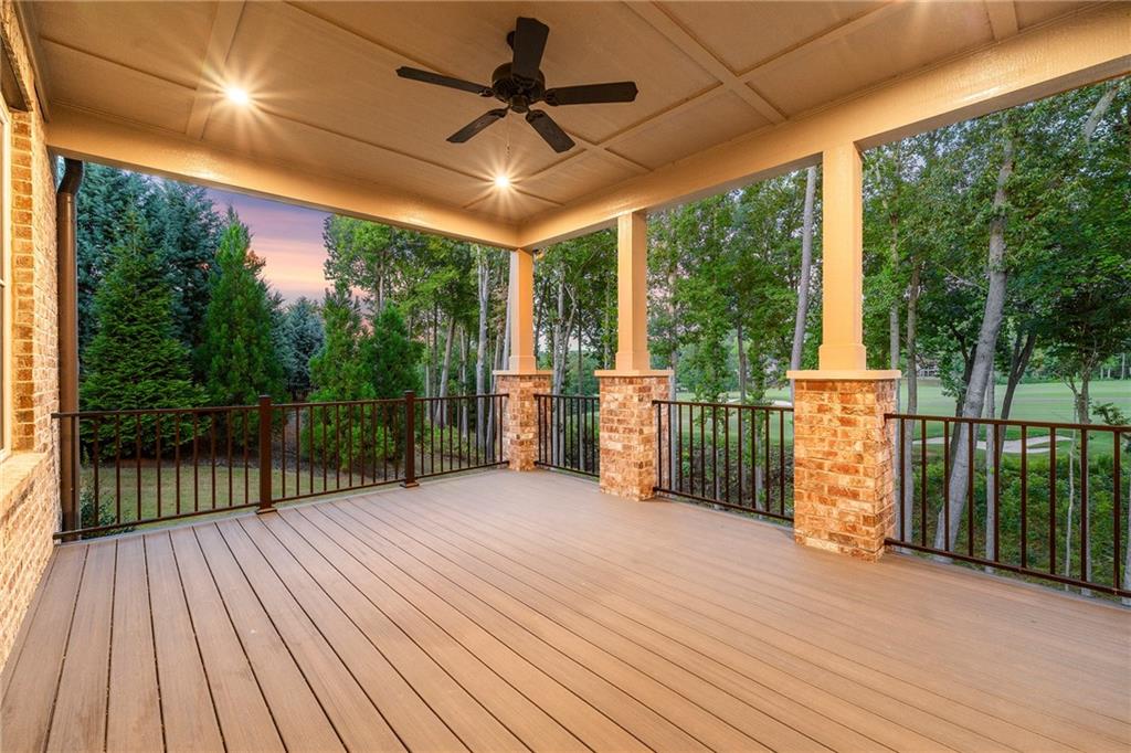 Covered wooden deck with brick columns and black railings overlooking trees at dusk.