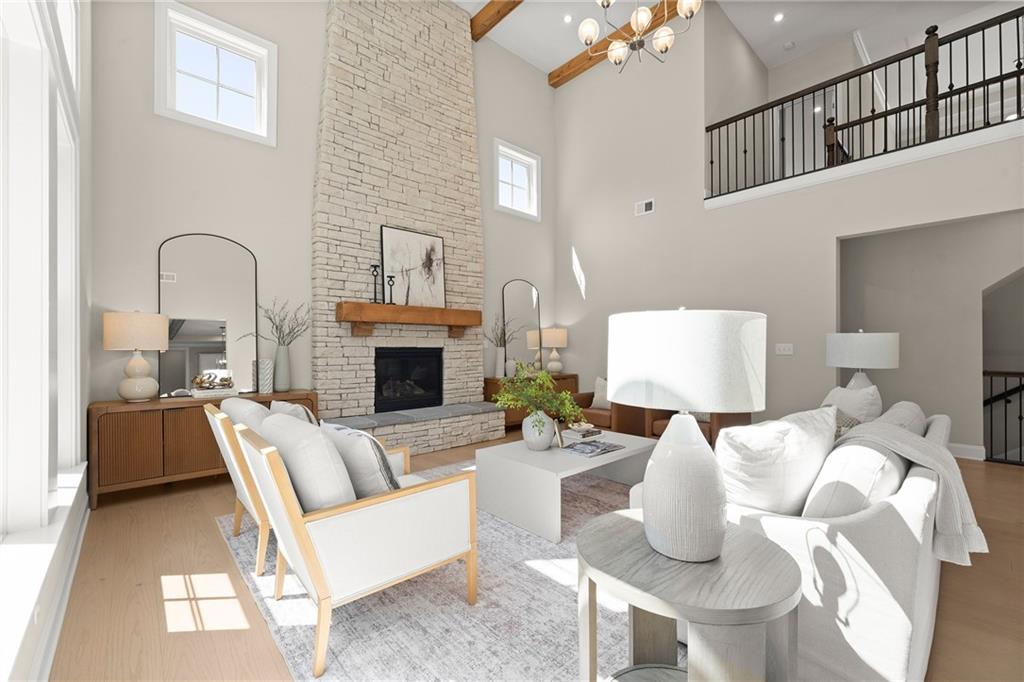 Double-height living room with a stone fireplace, exposed beam, and loft railing.