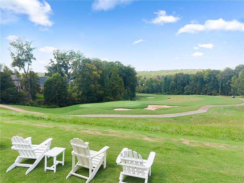 Golf course fairway with sand bunkers, seen from a lawn with three white Adirondack chairs.