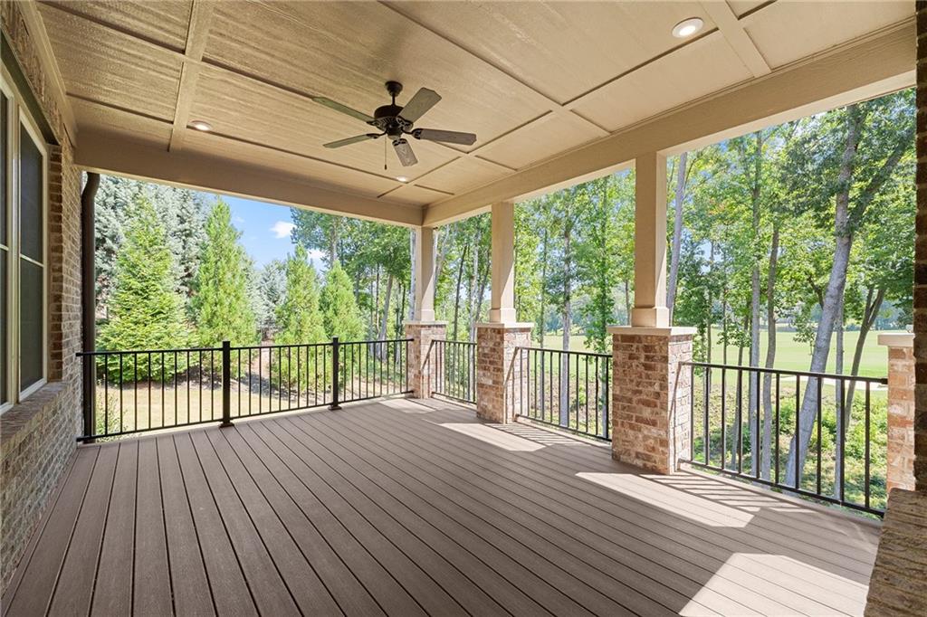 Covered porch with composite decking, ceiling fan, brick columns, and views of trees and lawn.