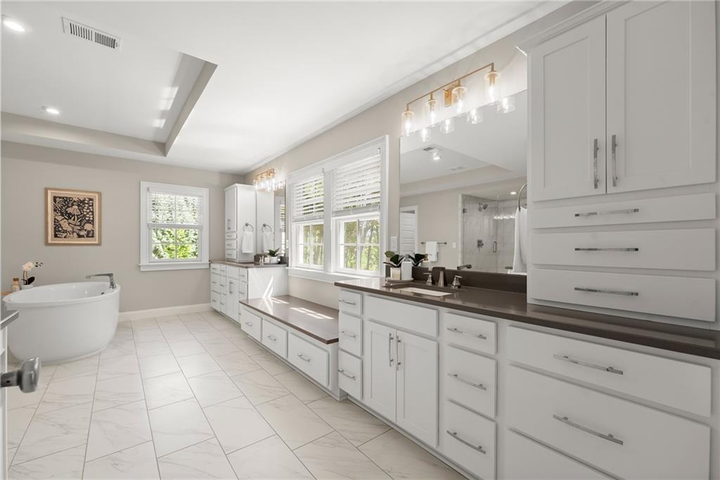 Bright bathroom with white cabinetry, long dark countertops, a soaking tub, and large windows.