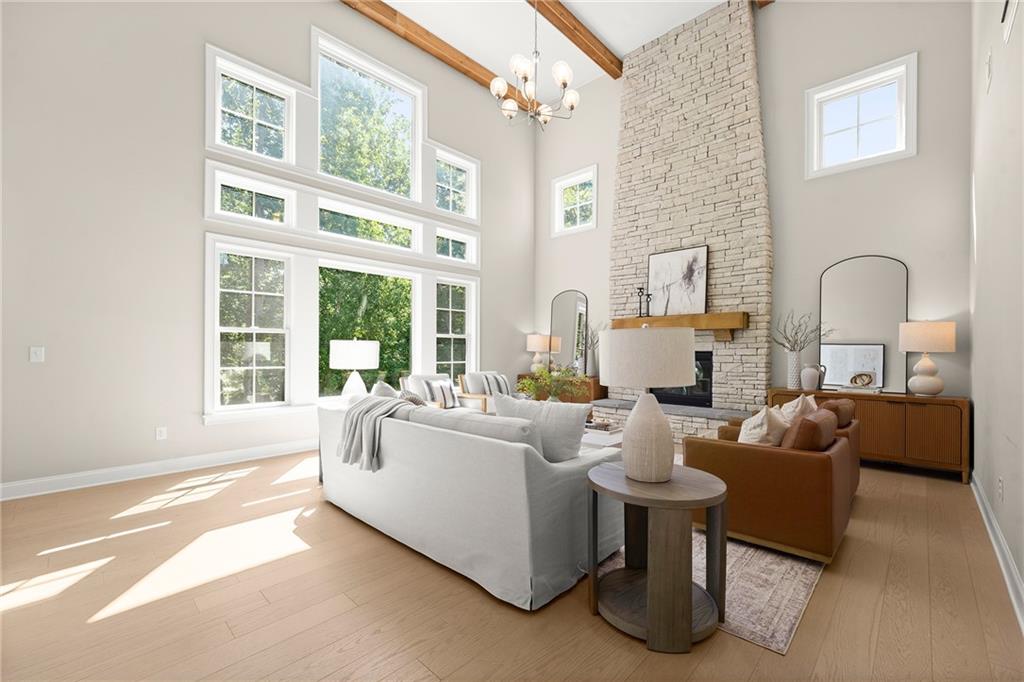 Staged living room with a stone fireplace, vaulted ceiling, exposed beams, and tall windows.