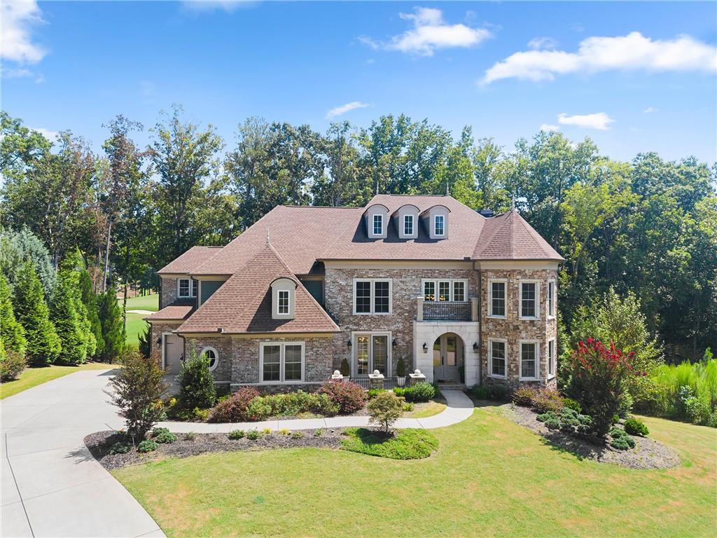 Large brick and stone home with three roof dormers, landscaped lawn, and curved driveway.