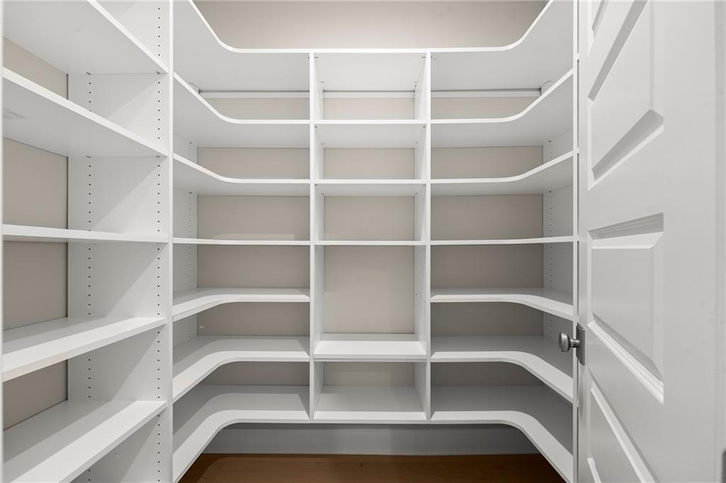 Walk-in closet with extensive white built-in shelving and hardwood flooring.