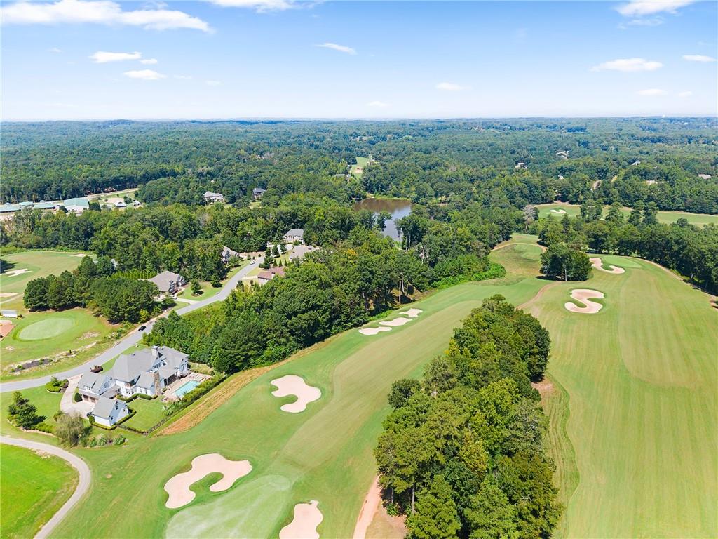 Aerial view of a home beside golf course fairways, sand bunkers, woods, and a pond.