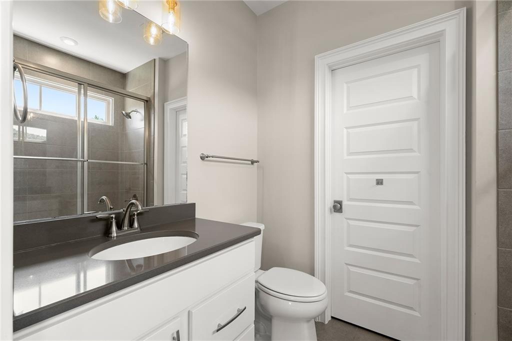 Bathroom with a white vanity and glass-enclosed gray-tile shower beside a high window.